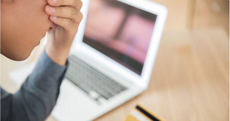 Utilizator stresat folosind laptopul pentru a raporta un cont fals care îi folosește fotografiile personale