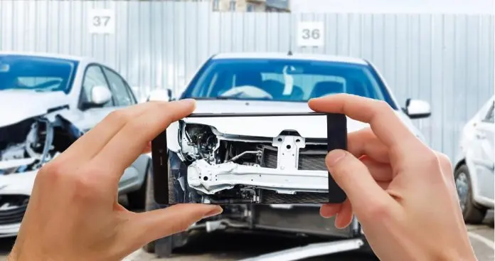 Contestare dauna totala auto asigurator RCA 2026 Un inspector de daune evaluând o mașină avariată grav cu o tabletă, cu un semn de daună totală pe ecran