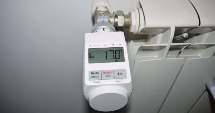 Repartitoare caldura obligatorii instalare lege 2026 O mână fixând un robinet termostatic pe un calorifer de apartament proaspăt dotat cu un repartitor electronic