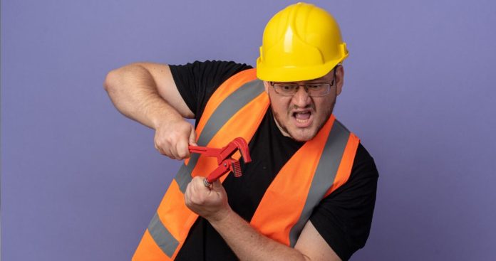 Un angajat cu brațul bandajat discutând cu un inspector ITM într-o hală de producție, având alături un dosar cu rapoarte de protecția muncii