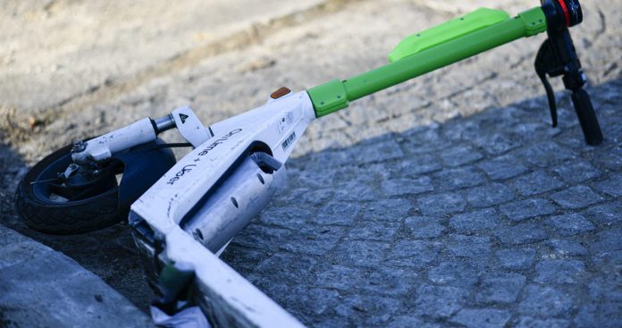 Un șofer fotografiind o trotinetă electrică căzută lângă portiera zgâriată a unei mașini parcate