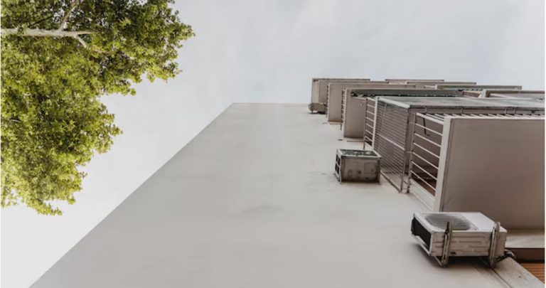 Instalator montând o unitate exterioară de aer condiționat pe fațada unui bloc de apartamente