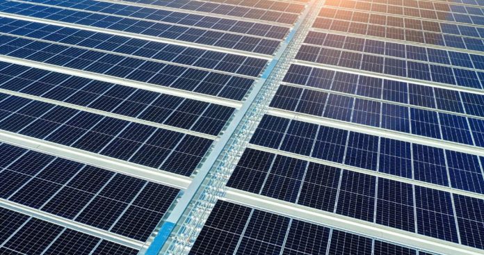 Un proprietar verificând un set de planuri urbanistice lângă o casă modernă cu panouri fotovoltaice instalate pe acoperiș