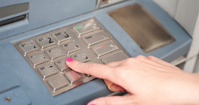 O persoană apropiind un smartphone cu ecranul luminos de cititorul contactless al unui bancomat modern