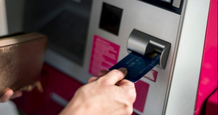 Un client îngrijorat stând în fața unui bancomat cu ecran de eroare, ținând telefonul în mână