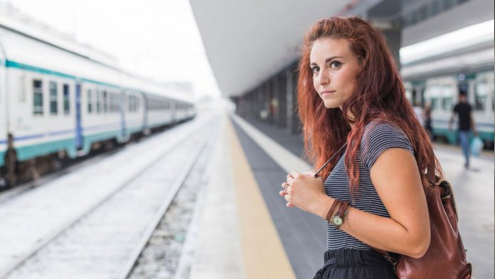 Un pasager asteptand in gara langa un ceas mare si un tren intarziat