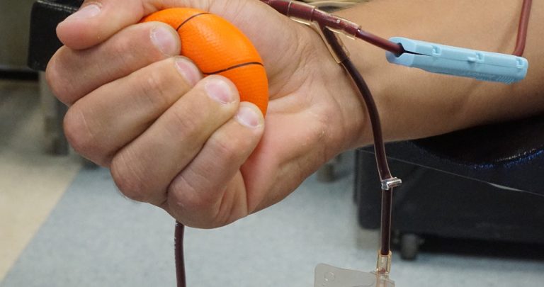 O asistentă medicală aplicând un bandaj pe brațul unui donator de sânge care ține în mâna liberă o adeverință și un card de tichete