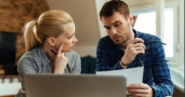 Un cuplu stresat verificând aplicația bancară pe telefon, având în față un document de la un executor judecătoresc