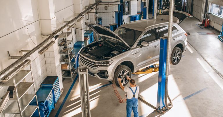 mecanic auto lângă o mașină cu capota ridicată în interiorul unui service