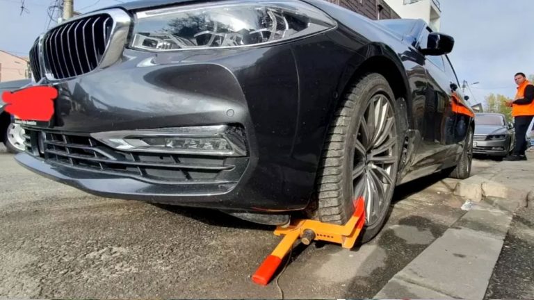 Roata unui autoturism blocată cu un dispozitiv galben tip caracatiță într-o parcare