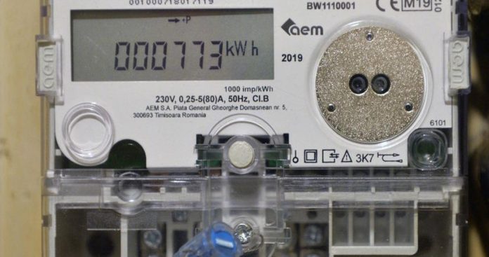 Un electrician autorizat purtând echipament de protecție, care instalează un contor electric inteligent cu afișaj digital pe un panou de distribuție