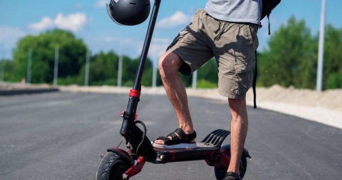 Un tânăr montând plăcuța cu numărul galben de înregistrare pe aripa din spate a unei trotinete electrice de mare putere