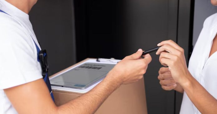 Un client deschizând un pachet de carton pentru verificare în fața unui curier care așteaptă cu POS-ul