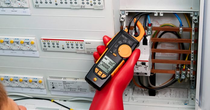 Electrician autorizat folosind un megohmetru portabil pentru a măsura un tablou electric într-o clădire de birouri comerciale