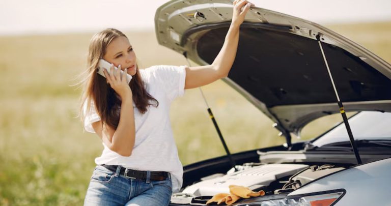 Un șofer dezamăgit stând cu mâinile în cap în fața unei mașini cu capota ridicată pe marginea autostrăzii