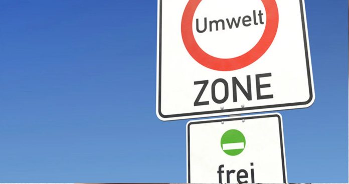 Un parbriz de autoturism pe care este lipită o vinietă ecologică verde Umweltplakette cu numărul de înmatriculare scris cu markerul