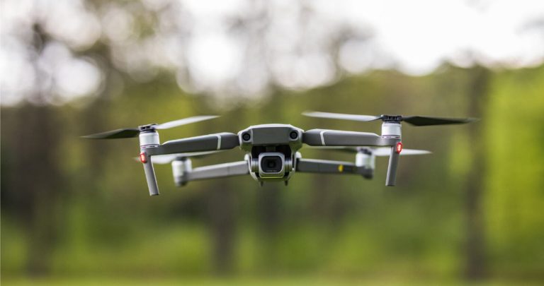 Un tânăr pilotând o dronă folosind o telecomandă cu ecran, având aplicația cu hărțile zonelor interzise deschisă pe telefon