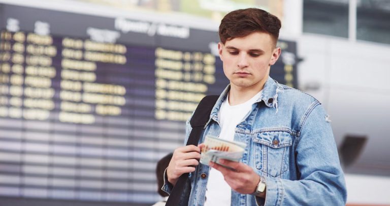 Pasager îngrijorat uitându-se la un panou de plecări din aeroport după ce a ratat zborul de legătură