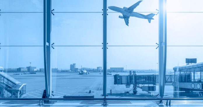 Un pasager dezamăgit uitându-se la un ecran de plecări din aeroport pe care scrie 'Poartă închisă' (Gate Closed), având biletul de avion și telefonul în mână