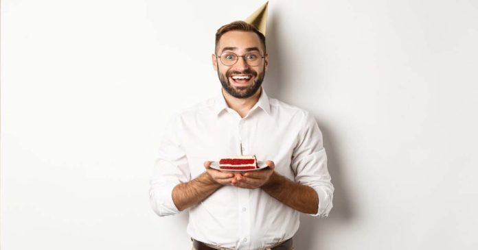 Bărbat zâmbind la petrecerea sa de aniversare lângă un tort festiv, ilustrând colecția de mesaje de la mulți ani pentru bărbați