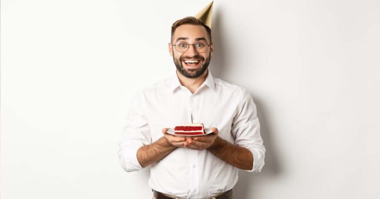 Bărbat zâmbind la petrecerea sa de aniversare lângă un tort festiv, ilustrând colecția de mesaje de la mulți ani pentru bărbați