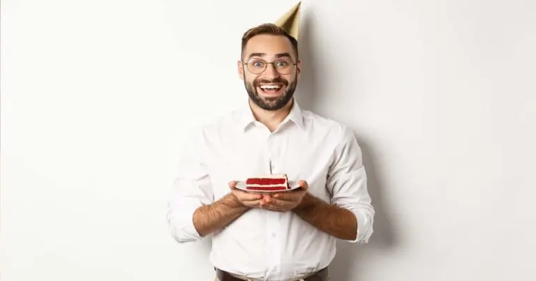 Bărbat zâmbind la petrecerea sa de aniversare lângă un tort festiv, ilustrând colecția de mesaje de la mulți ani pentru bărbați