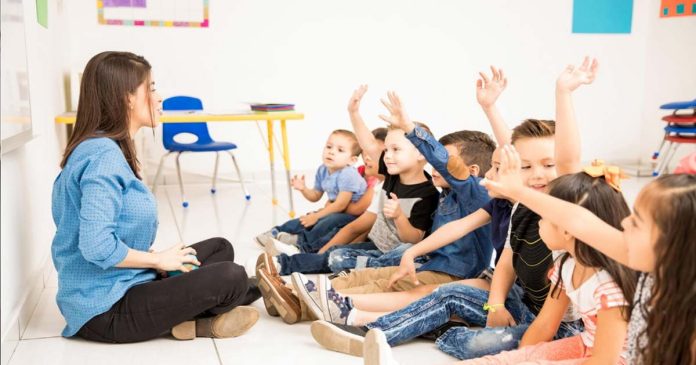 Copil fericit oferind un buchet de flori doamnei educatoare în sala de grupă, reprezentând un gest de mulțumire